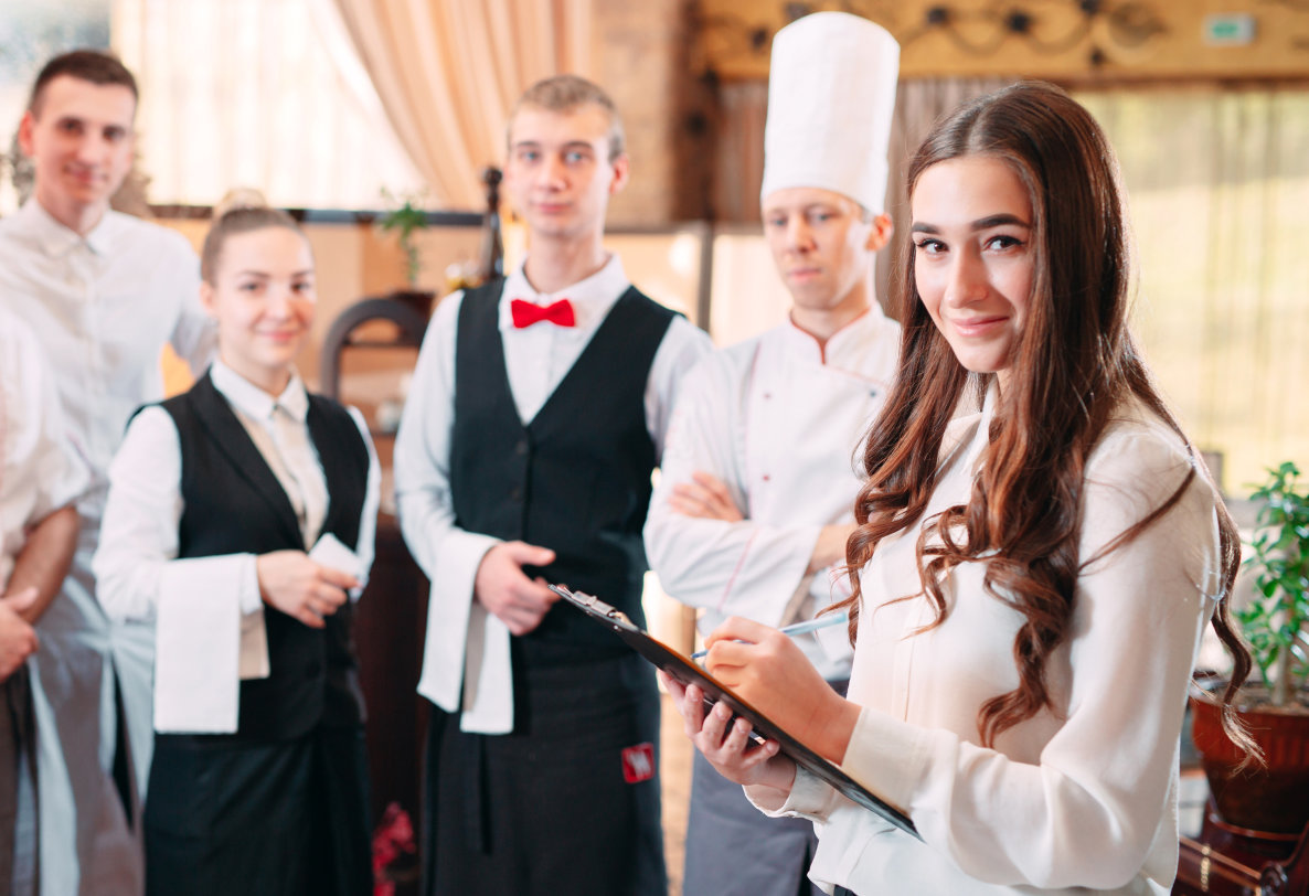 a young woman standing in front of a team of restaurant staff